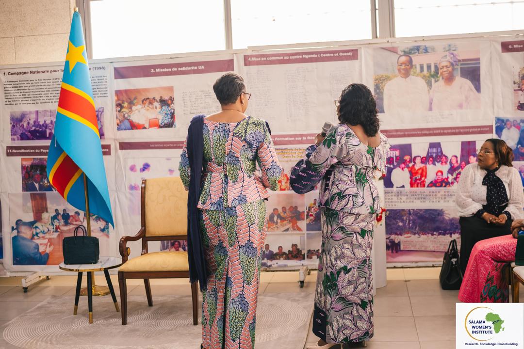 Deux femmes devant une exposition retraçant l'histoire des femmes, devant le drapeau de la RDC